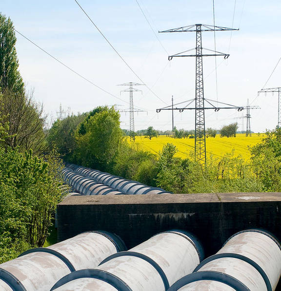 A number of high voltage lines across an open field with electric wires above